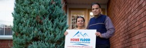 Home owners holding the Home Flood Protection Program sign outside of brick home
