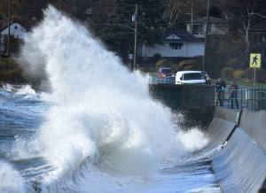 Pedestrians watch as huge waves break against the shoreline of McNeil Bay